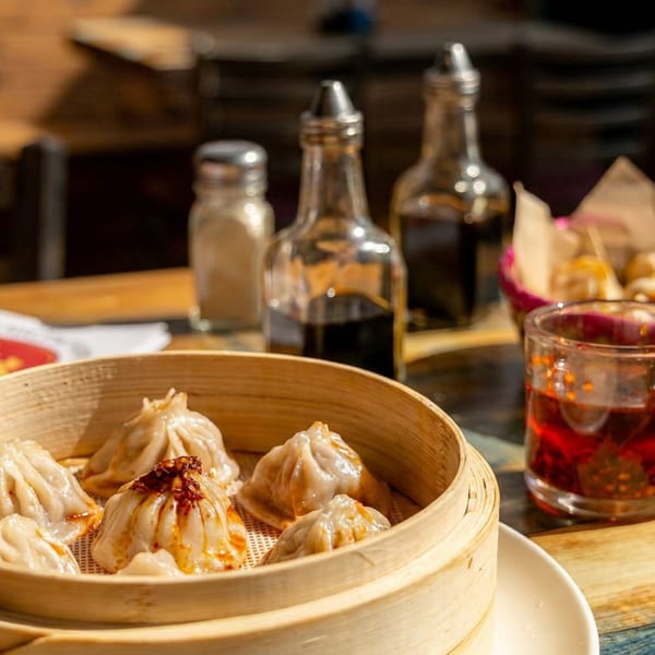 Freshly steamed dumplings in a bamboo basket with chili oil and condiments on a wooden table.