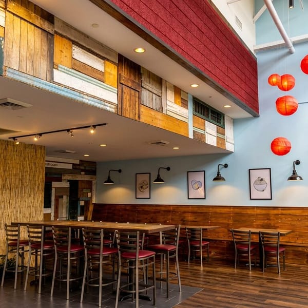 Vibrant restaurant interior with light blue walls, red lanterns, a neon dumpling sign, and wooden seating.
