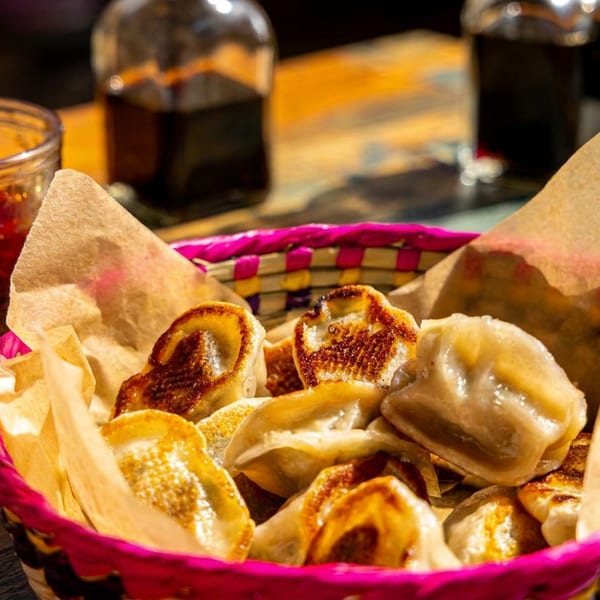 Crispy pan-fried dumplings in a pink basket with chili oil on a rustic wooden table.