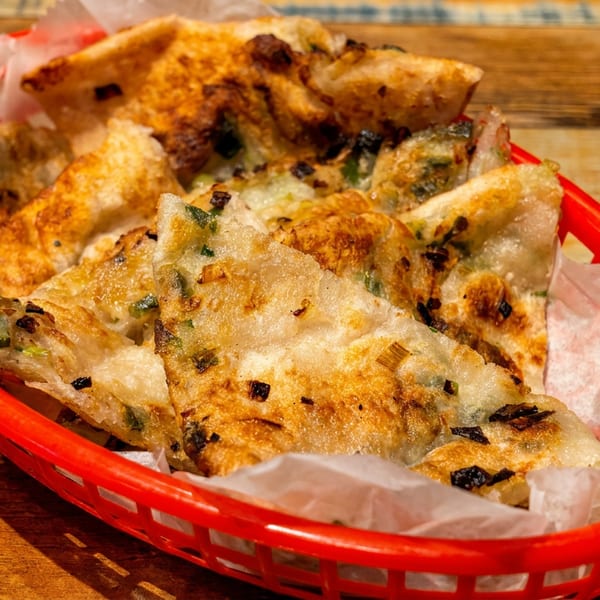 Golden-brown scallion pancakes in a red basket lined with white paper on a wooden surface.
