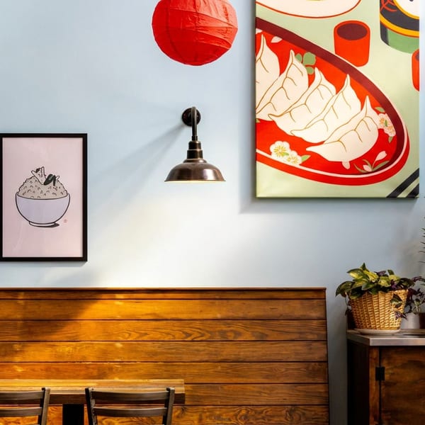 Cozy restaurant interior with light blue walls, wooden seating, Asian-themed art, and plants.