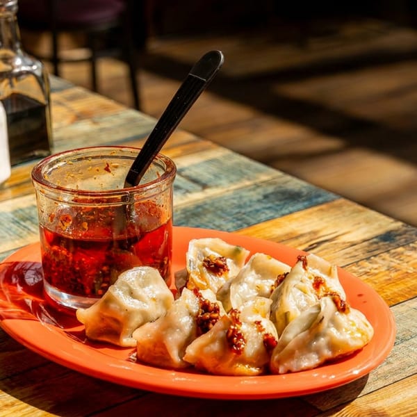 Steamed dumplings with chili oil and condiments on a colorful wooden table.