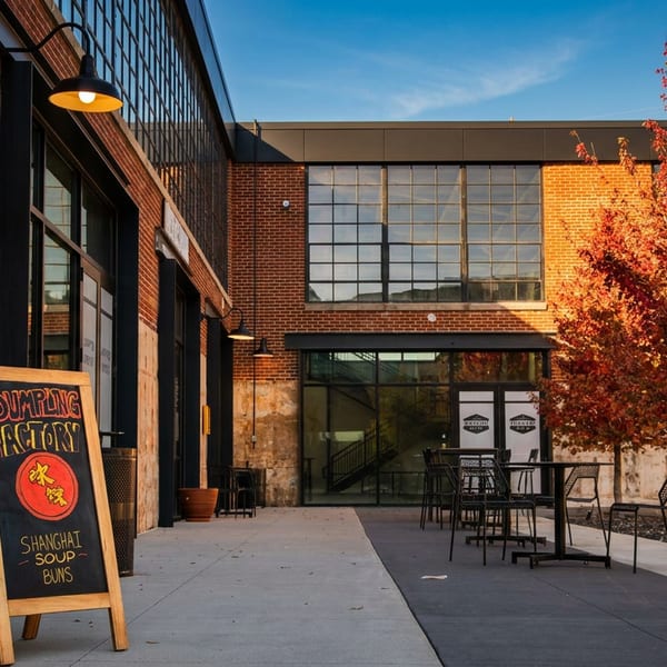 Dumpling Factory sign outside a brick building with outdoor seating and vibrant autumn trees under a blue sky.